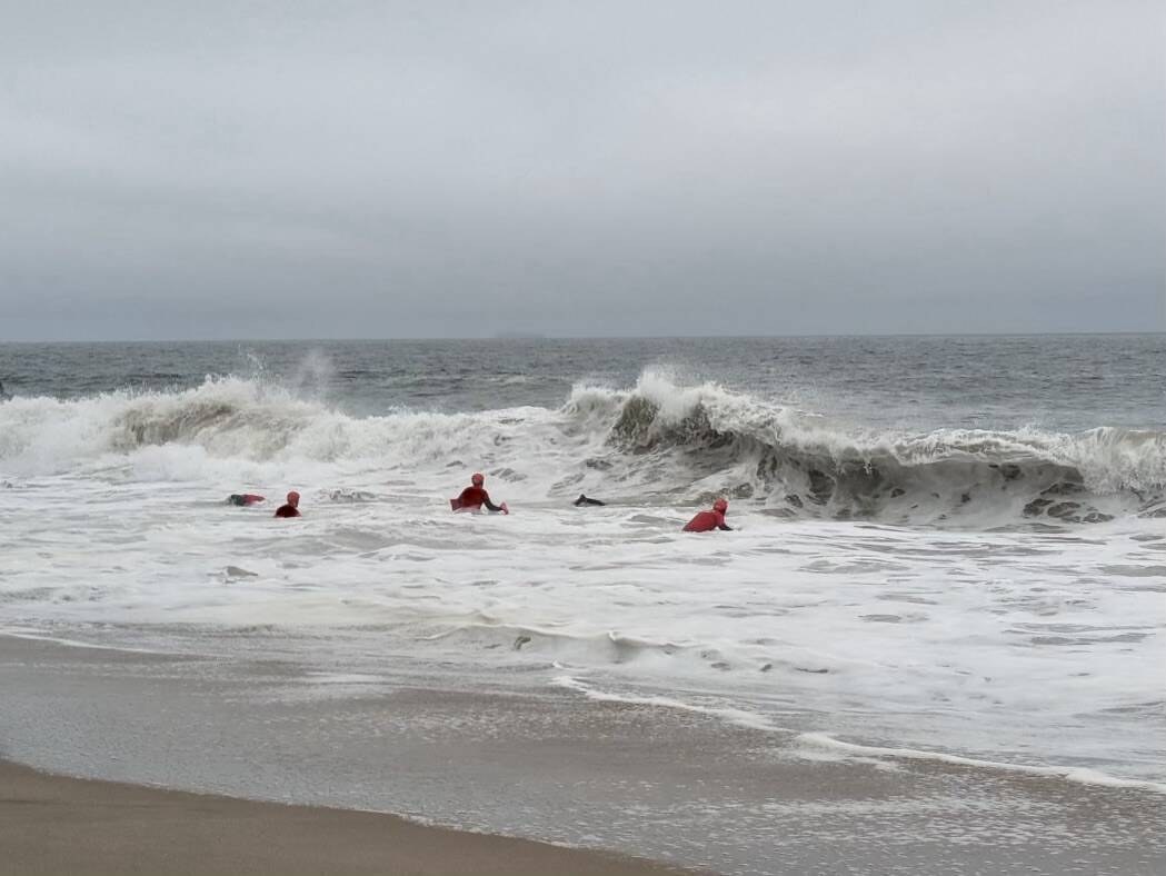 Ocean rescue trainees in red caps swimming through large surf at Point Mugu